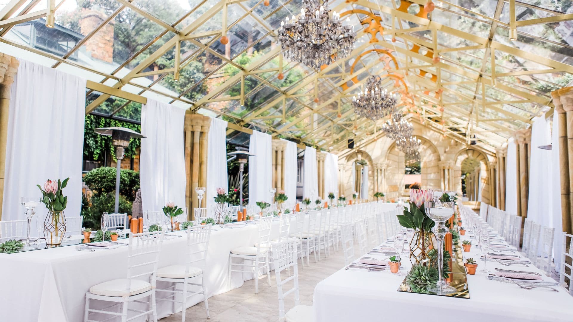 Une salle de réception dressée pour un mariage, sous une verrière